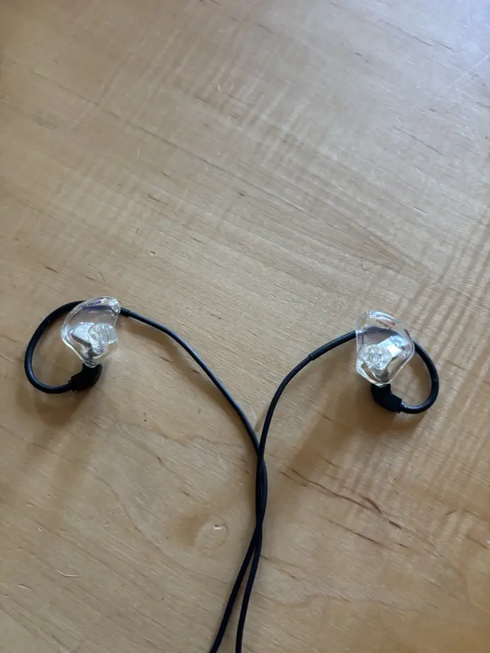 A pair of clear hard-acrylic Big Ear custom in-ear monitors on wood